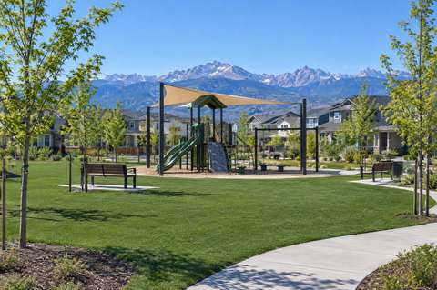 An HOA common area with artificial turf around a playground, benches and a walking path, mountains beyond