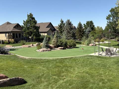 A backyard putting green ringed by boulders, evergreens and river rock, with flags in three cups, near Windsor, Colorado